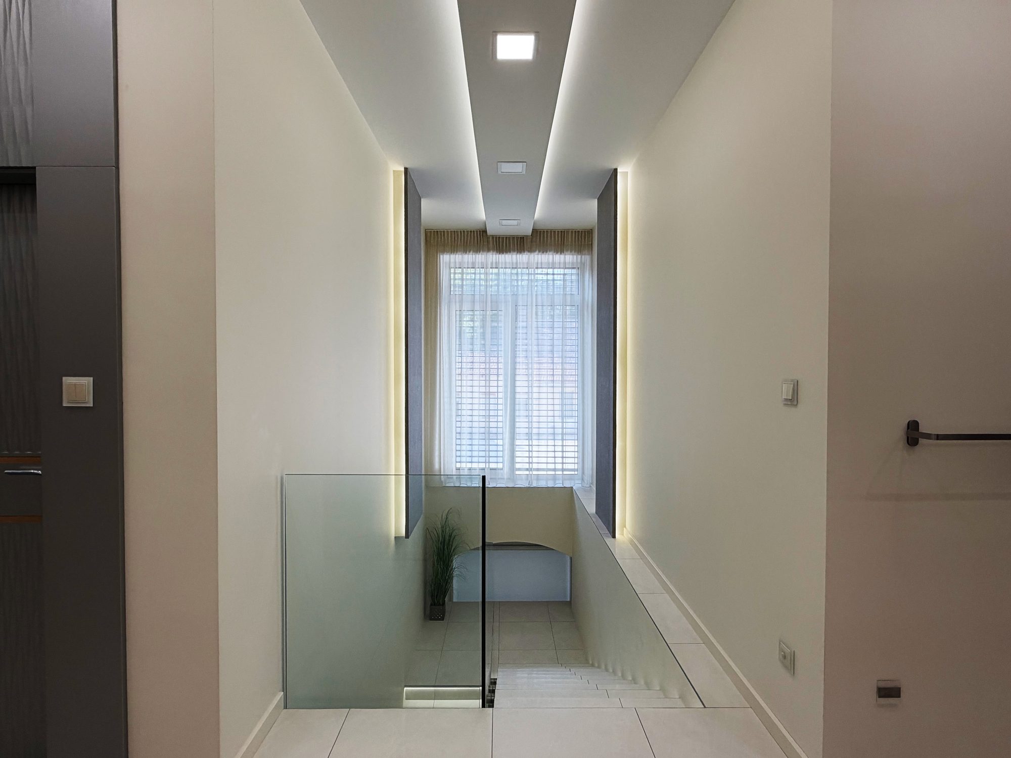 Hallway with a lit ceiling and glass balustrade, the staircase leading down